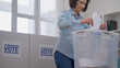 © Synthex🇺🇦 - Woman voting at a polling station and throwing a ballot into a box, election day, democracy