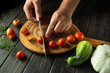 Wall Mural - A cook prepares a vegetable lunch on the kitchen table. Slicing cherry tomatoes before cooking. Tomato diet menu