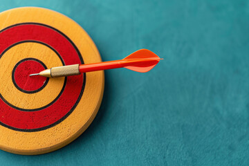 Red dart hitting the target center of a yellow and red bullseye on a teal background, symbolizing precision, goal achievement, and success.