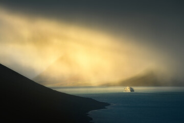 Tourist ship in a fjord in the Westfjords of Iceland on a stormy rainy day and dramatic sunlight