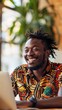 © Maria Mikhaylichenko - Joyful expression radiates from a man wearing vibrant African-inspired attire as he engages with a laptop, embodying positivity in a modern work setting.