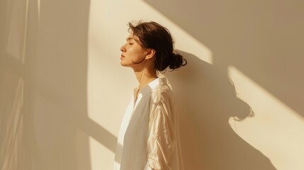 young woman wearing white shirt enjoying sun rays standing near wall