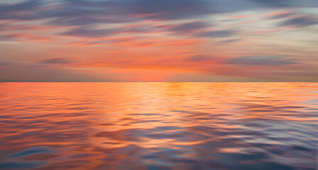 Poster - A beautiful sunset over the calm sea with red and orange clouds reflecting in the water