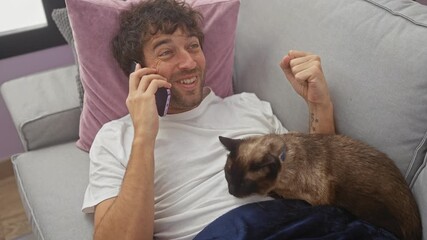 Wall Mural - A smiling man converses on a phone while petting a cat, illustrating a cozy indoor setting with comfortable furniture.