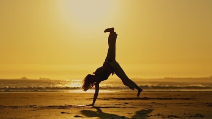 Wall Mural - A woman is practicing martial arts on a beach at sunset