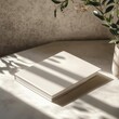 © Jayda_ArtistryHub - Close-up of a blank white book on a table with sunlight and greenery in the background.