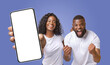 © Prostock-studio - A young black couple is excited about something they are looking at on a smartphone. The woman is pointing at the blank screen while the man has his fists pumped in the air, indicating excitement