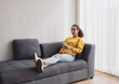 © Singh - Portrait latin american woman one person smile happy sitting sofa and looking television hand holding food and remote control in choosing to watch series on  most wonderful vacation day in living room