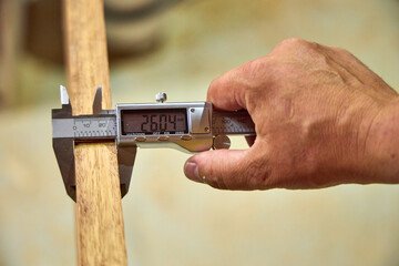 a man in a home carpentry workshop measures boards with a caliper close-up of hands