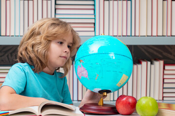 Fototapete - School kid pupil looking at globe in library at the elementary school. World globe. School child 7-8 years old with book go back to school. Little student.