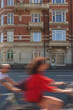 © Nibuya Qubik/Stocksy - A motion-blurred image of cyclists riding past a red brick building