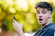 © carballo - young man or teenager on the street with mobile phone and surprised expression