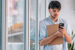 © carballo - young man with mobile phone and documents next to the window
