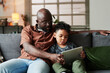© pressmaster - Adorable little boy and young African American man in casualwear looking at screen of tablet held by child while watching online movie