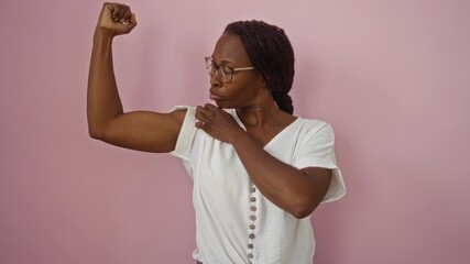 Sticker - Strong young african american woman with glasses standing confidently, showing arm muscle power over isolated pink background