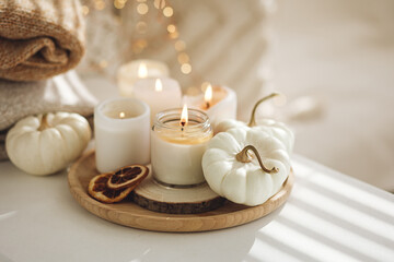 Atmospheric aroma candles with sweet spicy scent and white pumpkins on wooden tray, autumn bedroom decor. Autumn cozy home and hygge concept, place for relaxation, detention. Aromatherapy