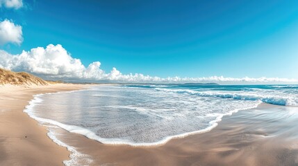 Wall Mural - Panoramic image of a sandy beach with sea waves gently rolling in, providing a broad and calming seaside view.