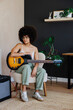 © BONNINSTUDIO/Stocksy - Female musician holding electric guitar taking break at home