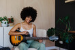 © BONNINSTUDIO/Stocksy - Woman with afro hairstyle playing electric guitar at home