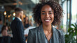 © khonkangrua - Confident businesswoman with curly hair smiles warmly in a modern office, reflecting professionalism and a positive work environment.