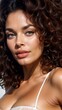 © Besler - A young woman with curly brunette hair. She is wearing a white bra and her hair is styled in loose curls that frame her face.