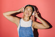 © VICTOR TORRES/Stocksy - Happy asian woman in denim overalls listening to music with headphones