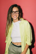 © VICTOR TORRES/Stocksy - Smiling woman in a stylish outfit with glasses on red background