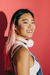 © VICTOR TORRES/Stocksy - Young asian woman with pink headphones smiling against a pink backdrop