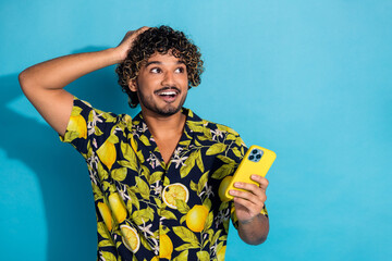 Poster - Photo of crazy man with wavy hairstyle dressed print shirt hold smartphone look at sale empty space isolated on blue color background