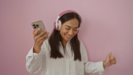 Canvas Print - Young woman with brunette hair wearing headphones and holding a smartphone over an isolated pink background, smiling and appearing happy