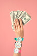 © Tatyana Lavrova/Stocksy - Hand Holding US Dollar Bills With Three Wristwatches on Pink Backdrop.