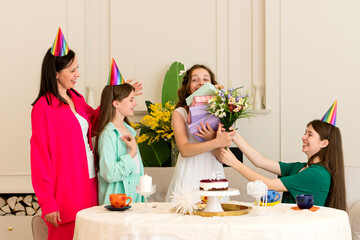 Birthday girl holds flowers and gifts while surrounded by family