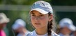 © Suphot - Focused young tennis player wearing a white cap during a sunny day training session, with players in the background.