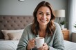 © ThomasLENNE - portrait of Smiling woman with coffee mug sitting on bed at home