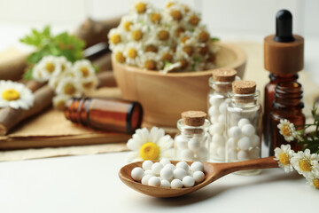 Wall Mural - Homeopathic remedy. Spoon with pills, bottles and chamomile flowers on white table, closeup