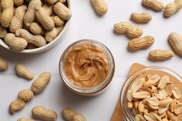 Poster - Tasty peanut butter in jar and groundnuts on white tiled table, flat lay