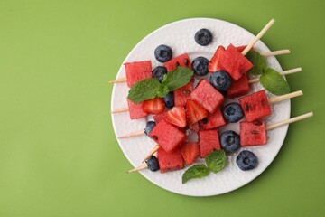 Poster - Skewers with tasty watermelon, strawberries, blueberries and mint on green table, top view. Space for text