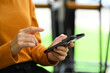 © Prathankarnpap - Cropped image of young woman dressed in orange turtleneck sweater using smartphone at office