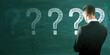 © Who is Danny - Back view of thoughtful young european male with chalk drawn question marks on blackboard background. Solution, education and knowledge concept.
