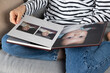 © Zarina Lukash - Woman looking at family photo album with her family and a baby