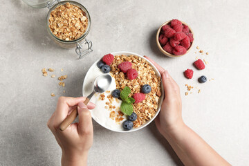 Wall Mural - Woman eating tasty granola with berries and yogurt at grey textured table, top view