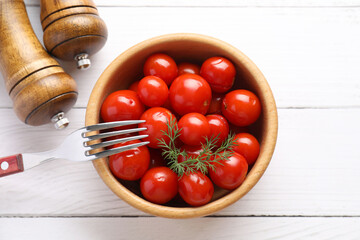 Tasty pickled tomatoes in bowl, dill and fork on white wooden table, top view