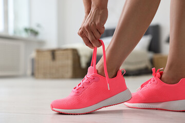 Wall Mural - Woman tying shoelace of pink sneaker indoors, closeup. Space for text