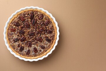 Wall Mural - Delicious pecan pie in baking dish on light brown background, top view. Space for text