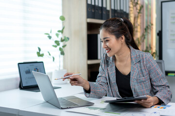 Wall Mural - A woman is sitting at a desk with a laptop and a tablet