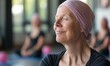 © Nadin Faust - close-up portrait of an elderly cancer survivor with a pink headscarf, smiling during a yoga class in the gym, focusing on relaxation techniques for coping