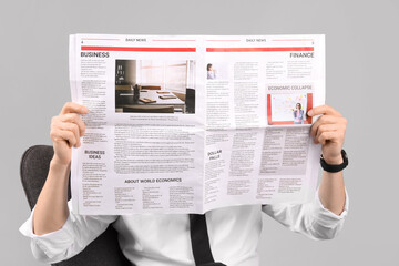 Wall Mural - Handsome businessman reading newspaper in armchair on grey background