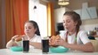 © maxximmm - children group eating fast food in the kitchen. delicious breakfast unhealthy food concept. children girls eat hamburgers and drink cola in the kitchen indoors lifestyle. fast food concept