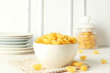 Bowl with raw conchiglie pasta on light background