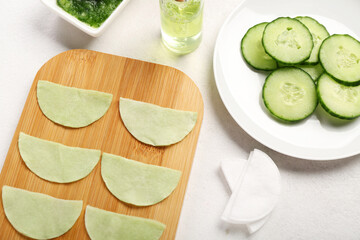 Wall Mural - Board with cotton under-eye patches and cucumber slices on white background, closeup